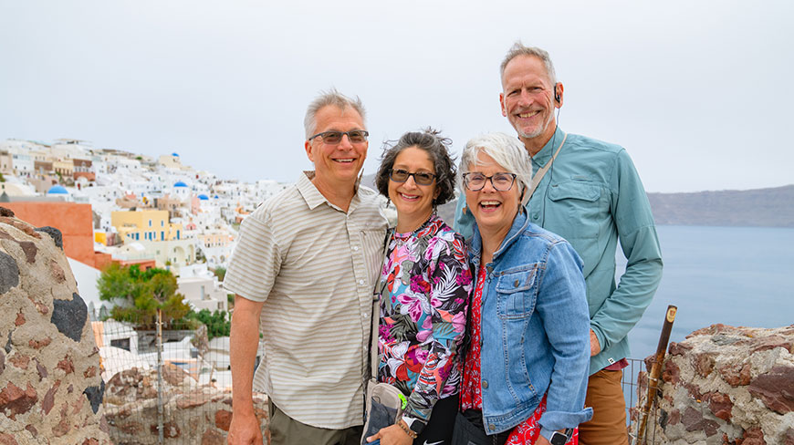 A group of four travelers smiles for a photo overlooking the white buildings of Santorini, Greece.