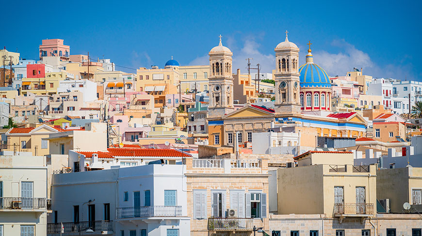 Colorful buildings and church domes pack a sunny hillside in Ermoupoli on the Greek island of Syros.