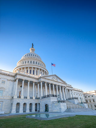 The United States Capitol Building in Washington, D.C., is viewed from the ground up against a clear, bright blue sky.