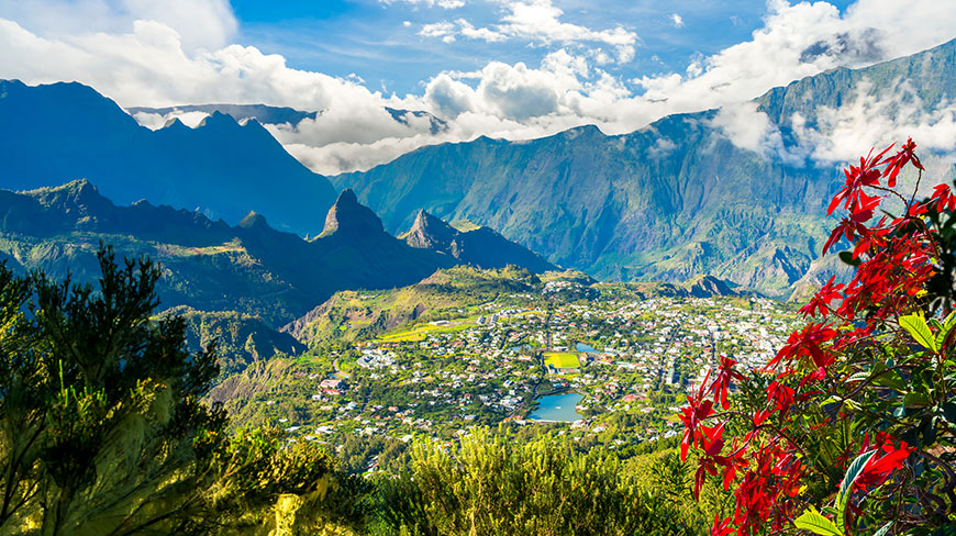 The town of Cilaos on Reunion Island, nestled in a valley surrounded by lush green mountains under a blue sky with white clouds.
