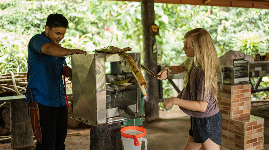 A man and a young girl press fresh sugarcane for juice at a family farm in Costa Rica.