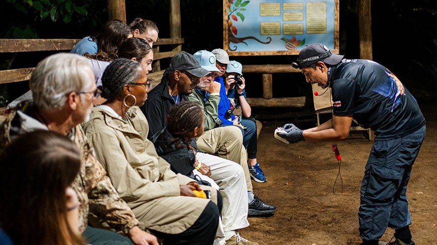 A guide in Costa Rica shows something small to a group of seated travelers during an evening presentation about bats.