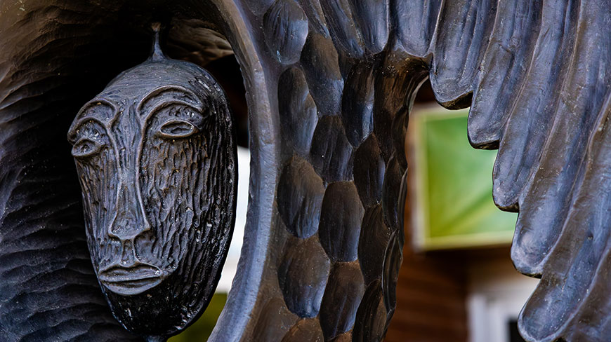 A close-up of a dark, textured, carved Indigenous mask with wing-like details at the Alaska Native Heritage Center.