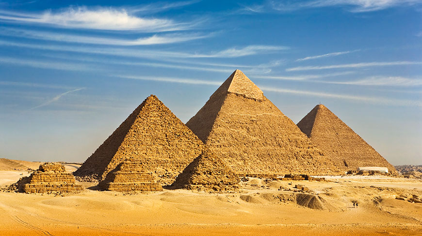 The Great Pyramids of Giza stand tall in the Egyptian desert under a bright blue sky with wispy clouds.