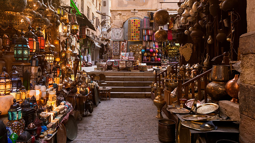 A narrow cobblestone alley in a Cairo bazaar in Egypt is lined with shops selling ornate, glowing lanterns and traditional brass goods.