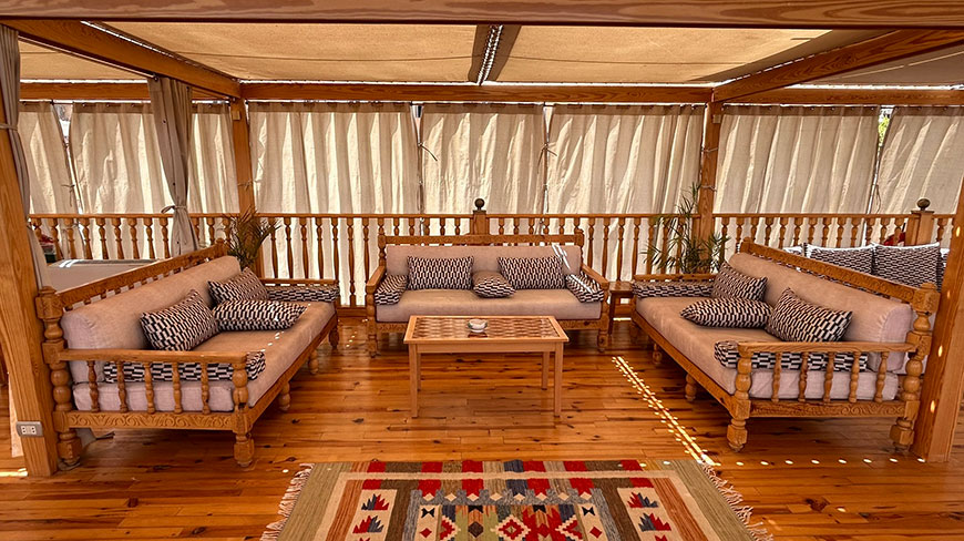 A shaded outdoor sitting area on a dahabeya boat in Egypt features wooden couches with patterned pillows on a wood deck.