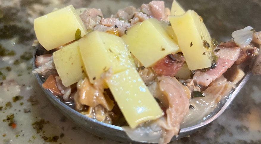 A close-up spoonful of Chincoteague, Virginia clam chowder with chunks of potatoes, clams, and herbs.