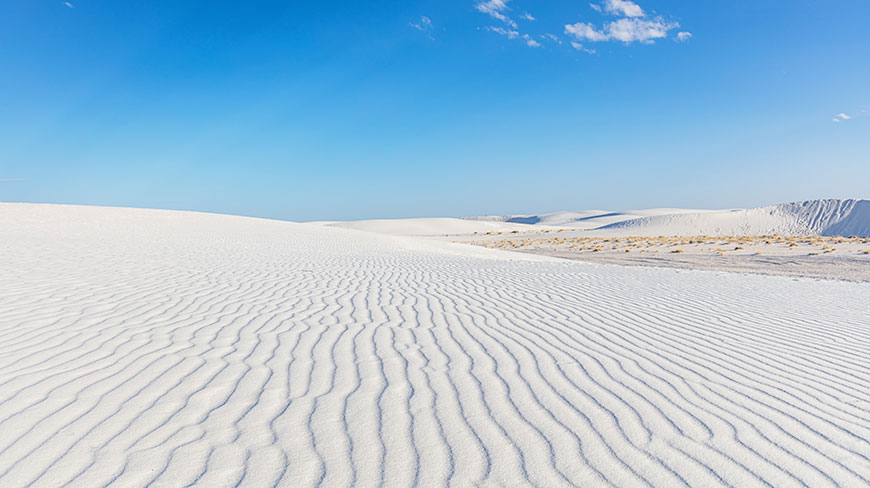 Wind-rippled white sand dunes at White Sands National Park in New Mexico under a vast, clear blue sky.