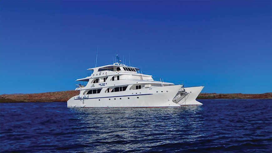 The white Tip Top V catamaran motors through the deep blue waters of the Galápagos Islands under a clear sky.