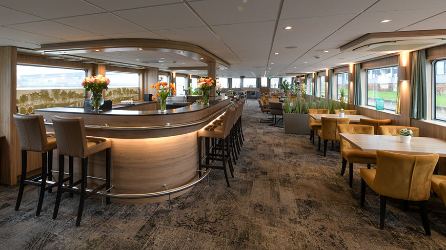 The modern bar and dining area aboard the De Holland ship in the Netherlands, featuring a curved wooden bar and mustard-yellow dining chairs.