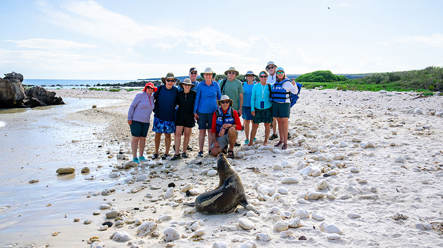 A group of tourists poses with a sea lion on a rocky beach in the Galápagos Islands.