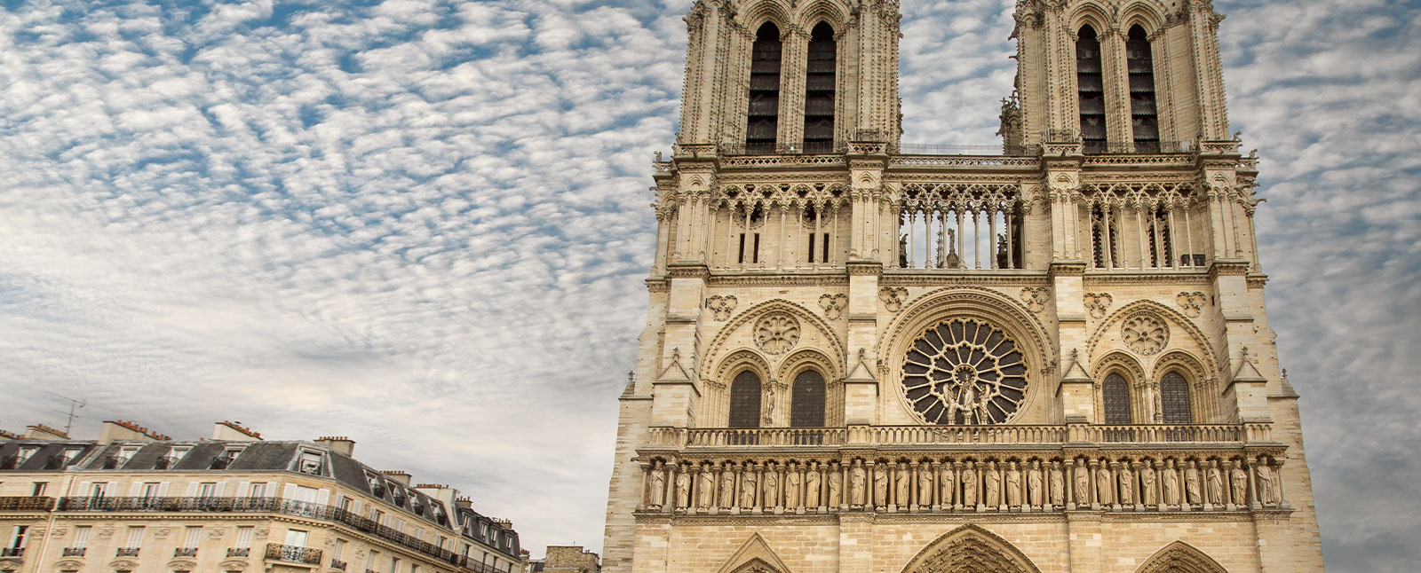 Close-up of the ornate Gothic facade of Notre-Dame Cathedral in Paris, France, set against a dramatic, cloud-filled sky.