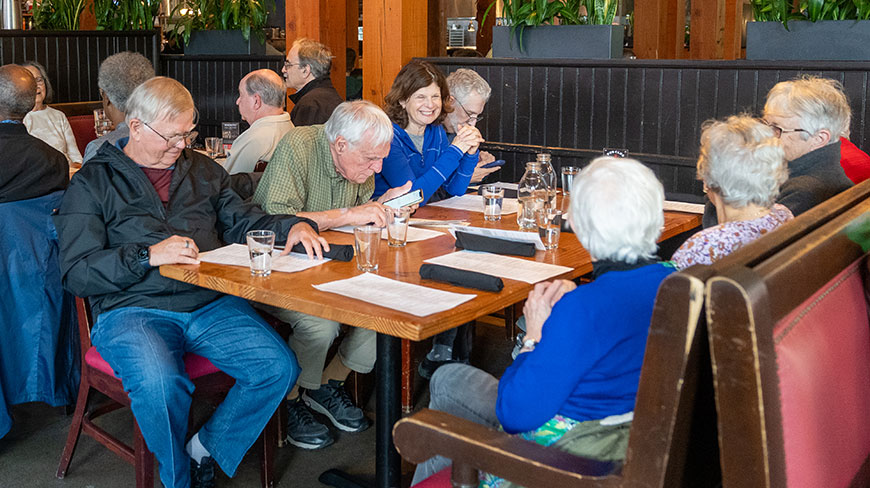 A group of older adults are seated and talking at a long dining table in a Washington, D.C. restaurant.