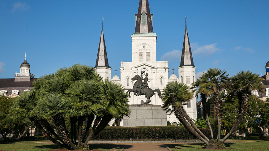 The Andrew Jackson statue in front of St. Louis Cathedral in Jackson Square, New Orleans, Louisiana, is framed by lush green palm trees.