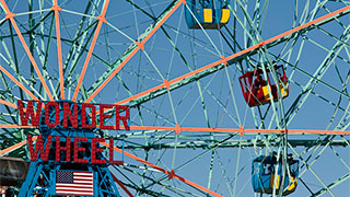 A close-up of the bright blue and orange structure of the Wonder Wheel ferris wheel at Coney Island, with red and blue gondolas.