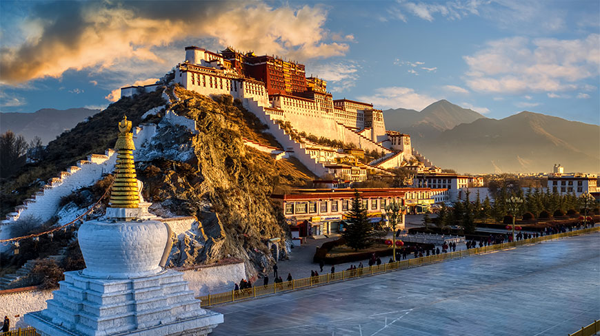 The Potala Palace in Tibet at sunset, with a golden stupa in the foreground and mountains rising in the distance.