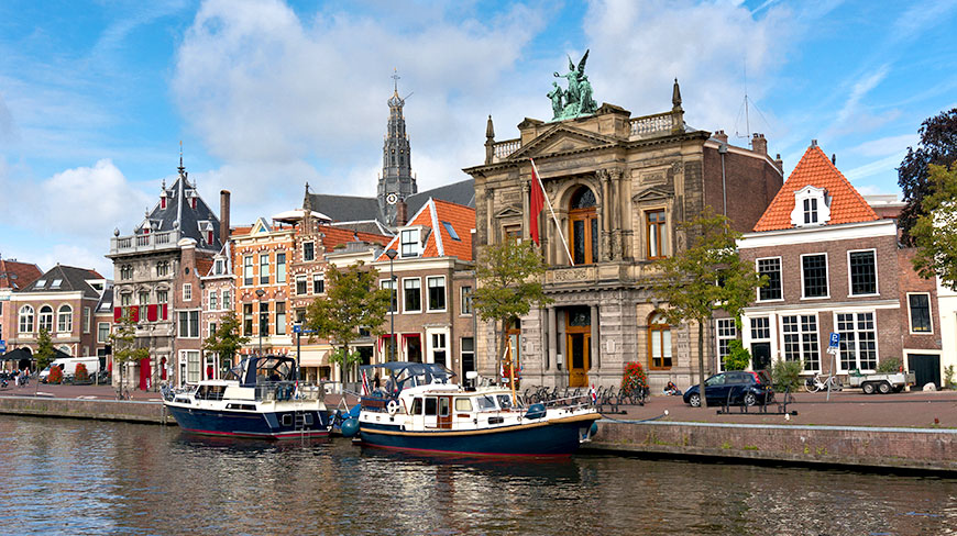 Boats are docked along a canal in front of the historic Teylers Museum and other traditional Dutch buildings in Haarlem, Netherlands.