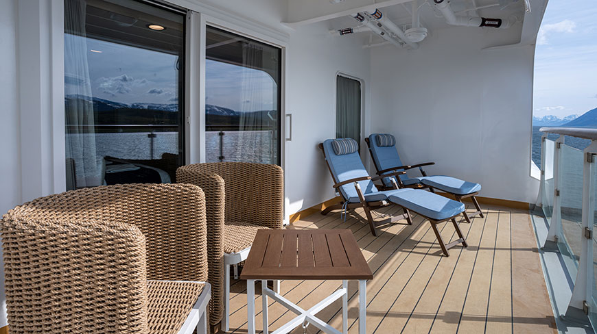 A private balcony on the Ocean Albatros ship with wicker chairs and loungers overlooking the snow-capped mountains of Antarctica.