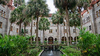 A stone bridge crosses a fountain in the lush, tropical courtyard of the Lightner Museum in St. Augustine, Florida.