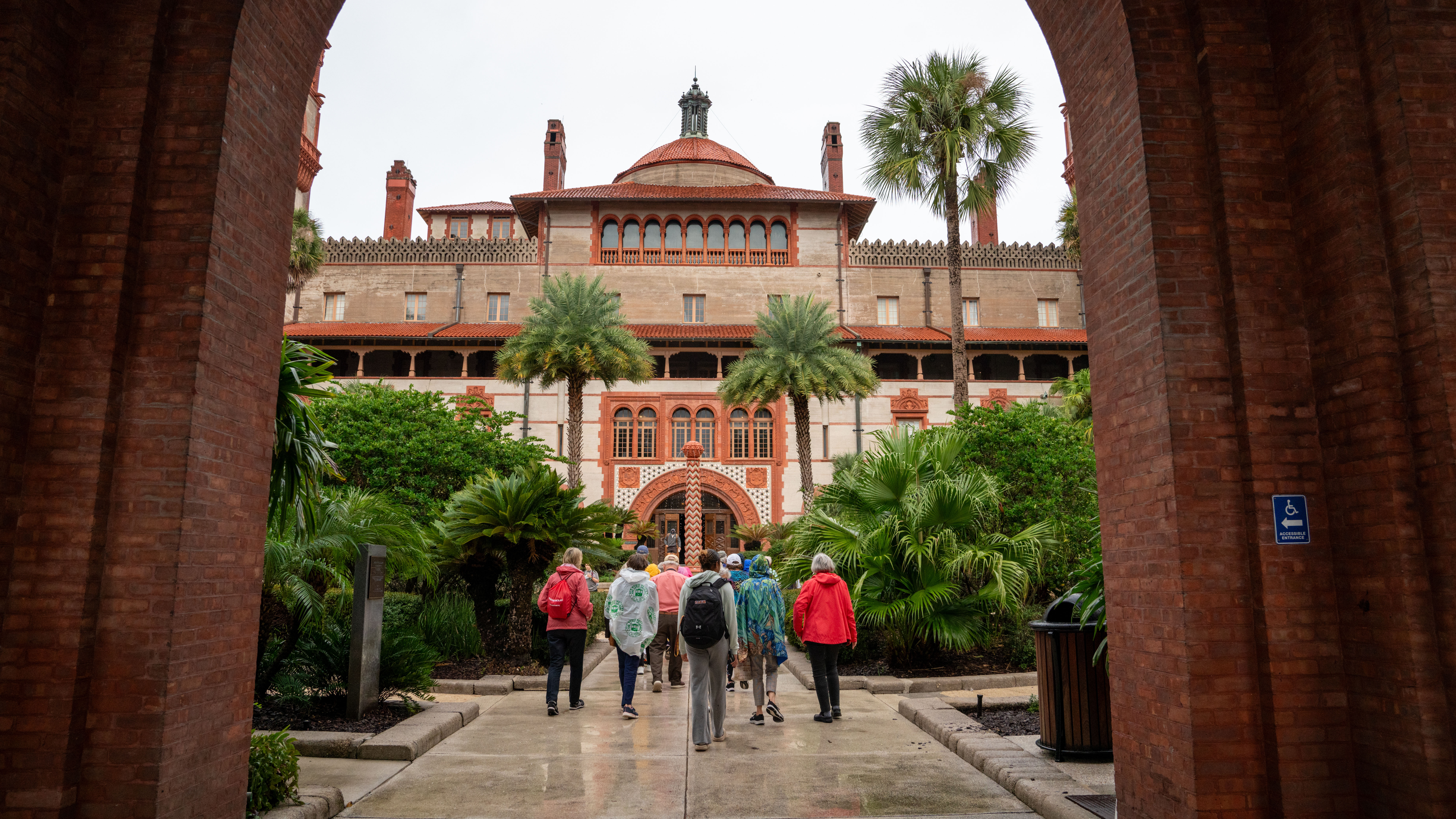 A group of people walks through a brick archway towards the grand Flagler College building in St. Augustine, Florida.