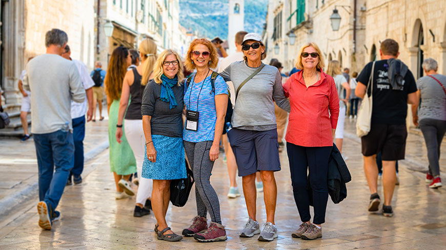 Four women smile for a photo on a busy stone street in Dubrovnik, Croatia.