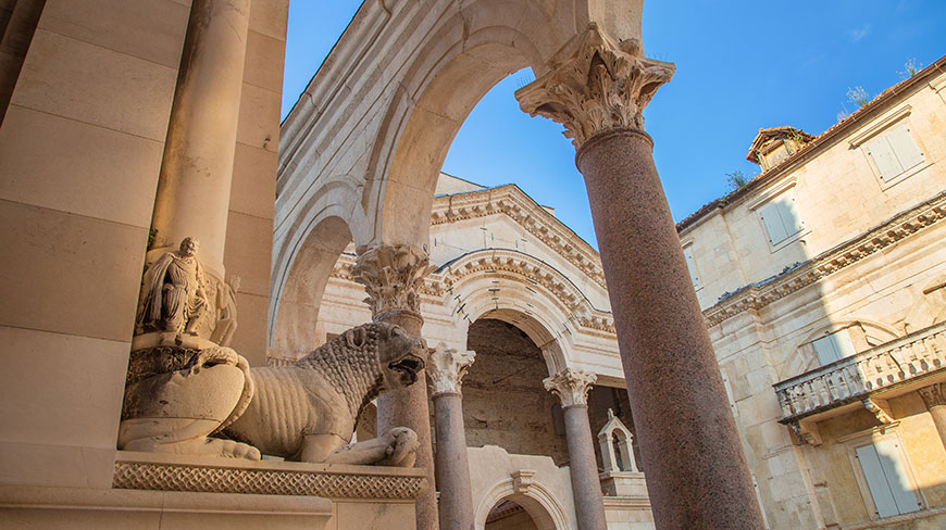 Ancient stone columns and a lion statue at Diocletian's Palace in Croatia under a clear blue sky.