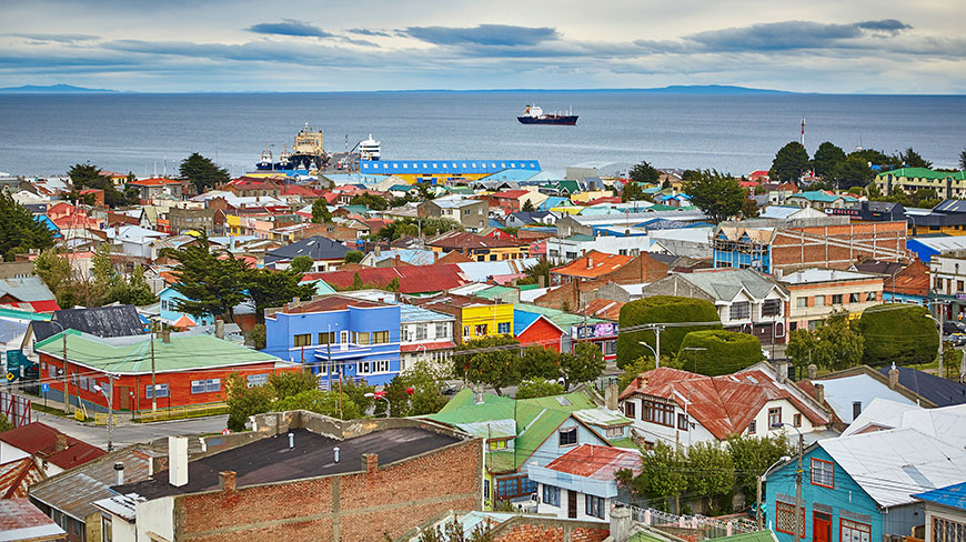 An aerial view of the colorful rooftops of Punta Arenas, Chile, with a large ship in the harbor under an overcast sky.