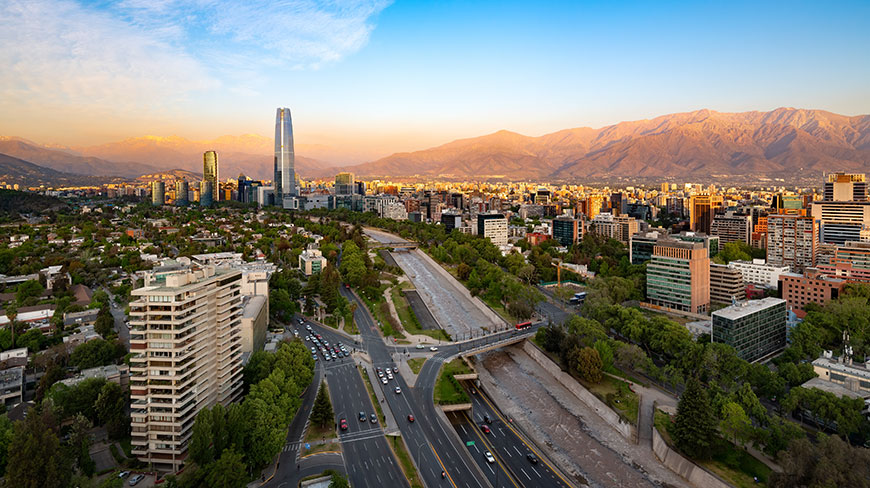 An aerial view of the Santiago, Chile skyline, with modern buildings and highways set against the Andes mountains at sunset.