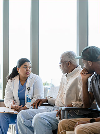 A female doctor consults with an older patient and a younger man in a well-lit hospital waiting area.