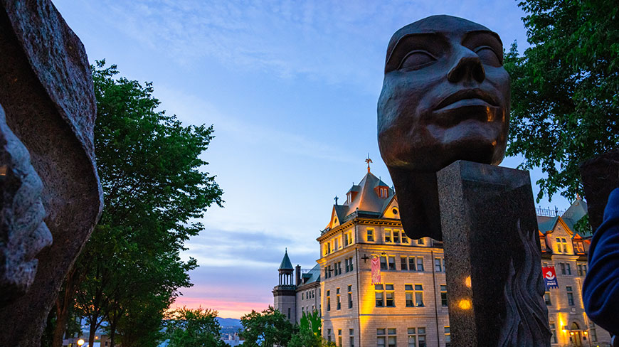 A large sculpture of a face in Old Quebec City, Canada, with a historic building in the background at dusk.