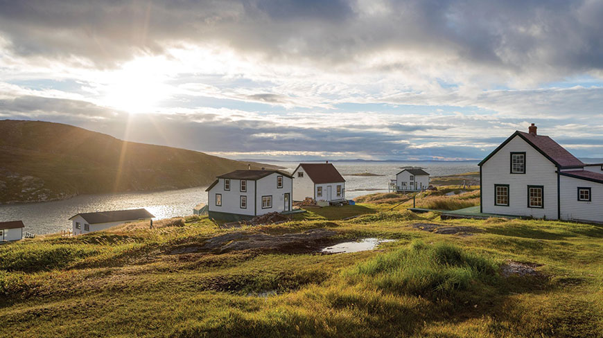 White houses sit on a grassy hill overlooking the water at sunset in Battle Harbour, Newfoundland and Labrador.