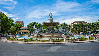 The large, ornate Rotunda Fountain in a roundabout in Provence, France, under a blue sky with some clouds.