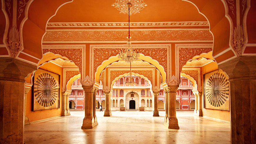 The ornate, orange-hued interior courtyard of the City Palace Museum in Jaipur, India, with detailed archways and a central chandelier.