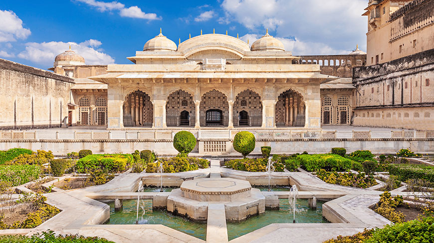 A star-shaped fountain sits in a lush garden courtyard before the ornate, domed architecture of Amber Fort in India.