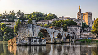 The famous Pont Saint-Bénézet stretches partially across the Rhône river in Avignon, France, with the Palais des Papes in the background.
